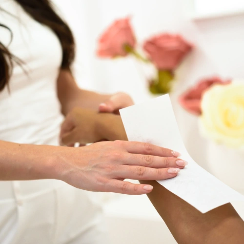 Woman having hair removal procedure on arms applying wax strip